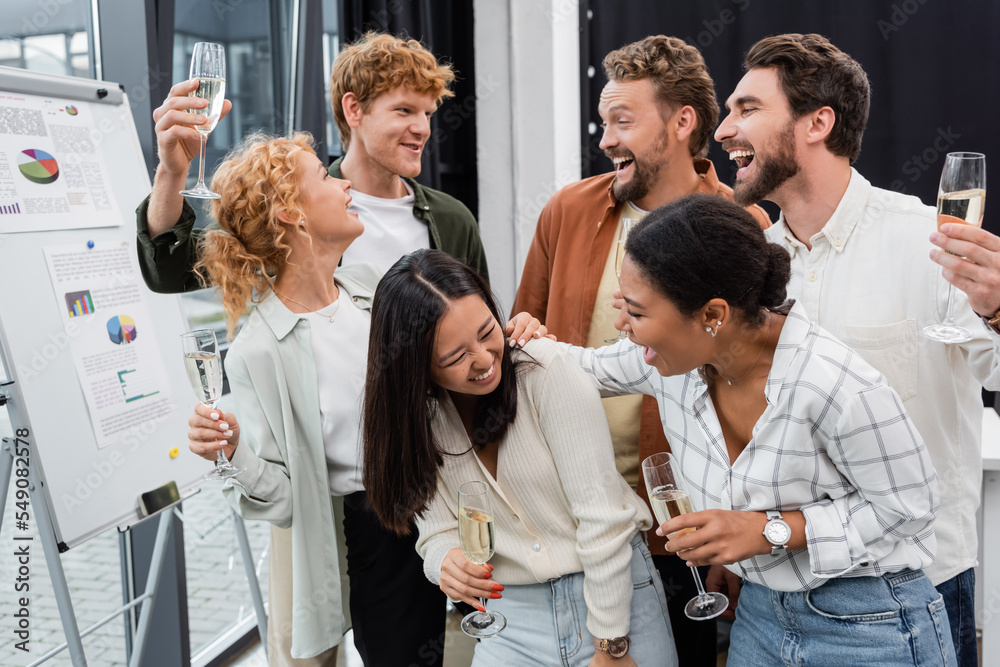 Cheerful multiethnic business people talking and holding glasses of champagne in office Cheerful multiethnic business people talking and holding glasses of champagne in office
