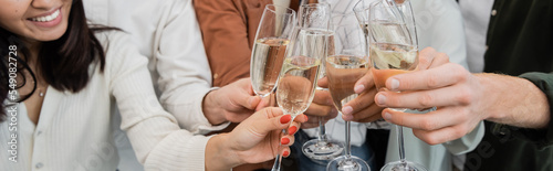 Cropped view of interracial business people clinking glasses of champagne in office, banner