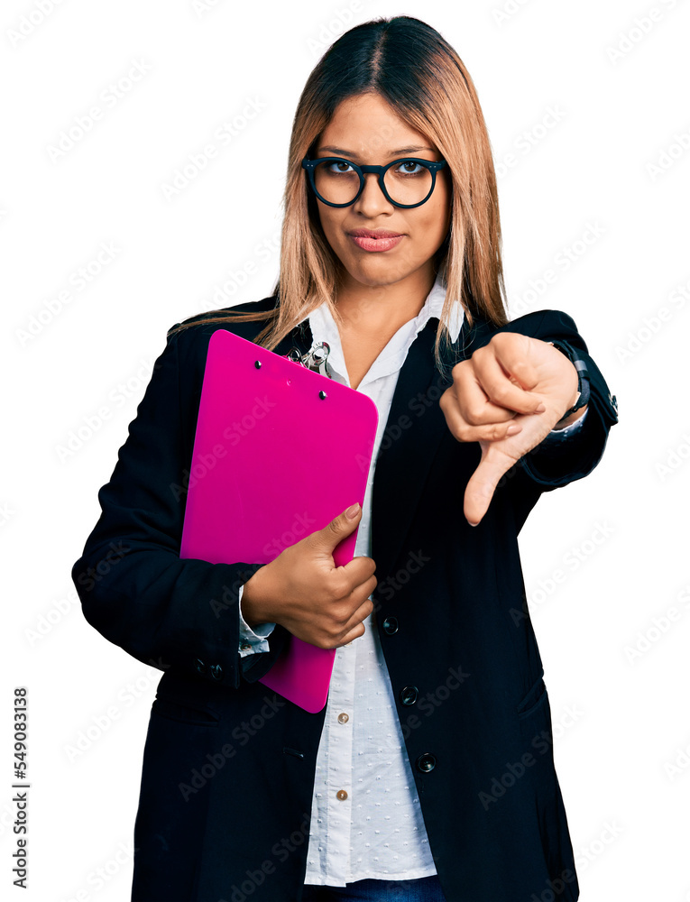 Young hispanic business woman holding clipboard with blank space looking unhappy and angry showing rejection and negative with thumbs down gesture. bad expression.