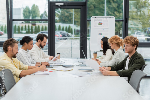 multiethnic business people working with gadgets and documents at conference table in office