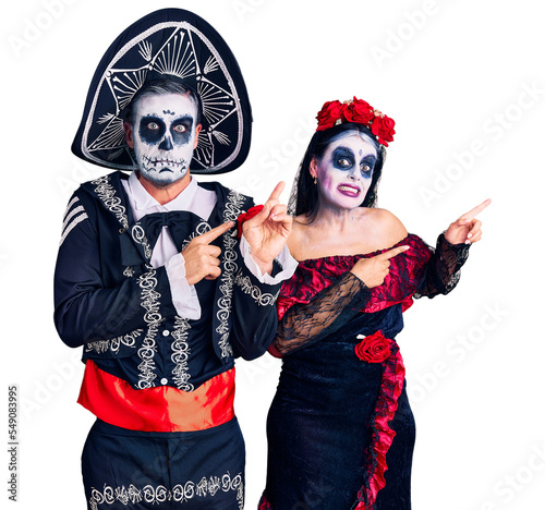 Young couple wearing mexican day of the dead costume over background pointing aside worried and nervous with both hands, concerned and surprised expression
