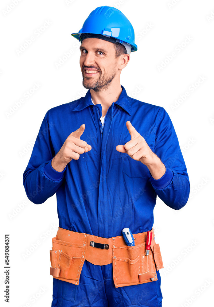 Young handsome man wearing worker uniform and hardhat pointing fingers to camera with happy and funny face. good energy and vibes.