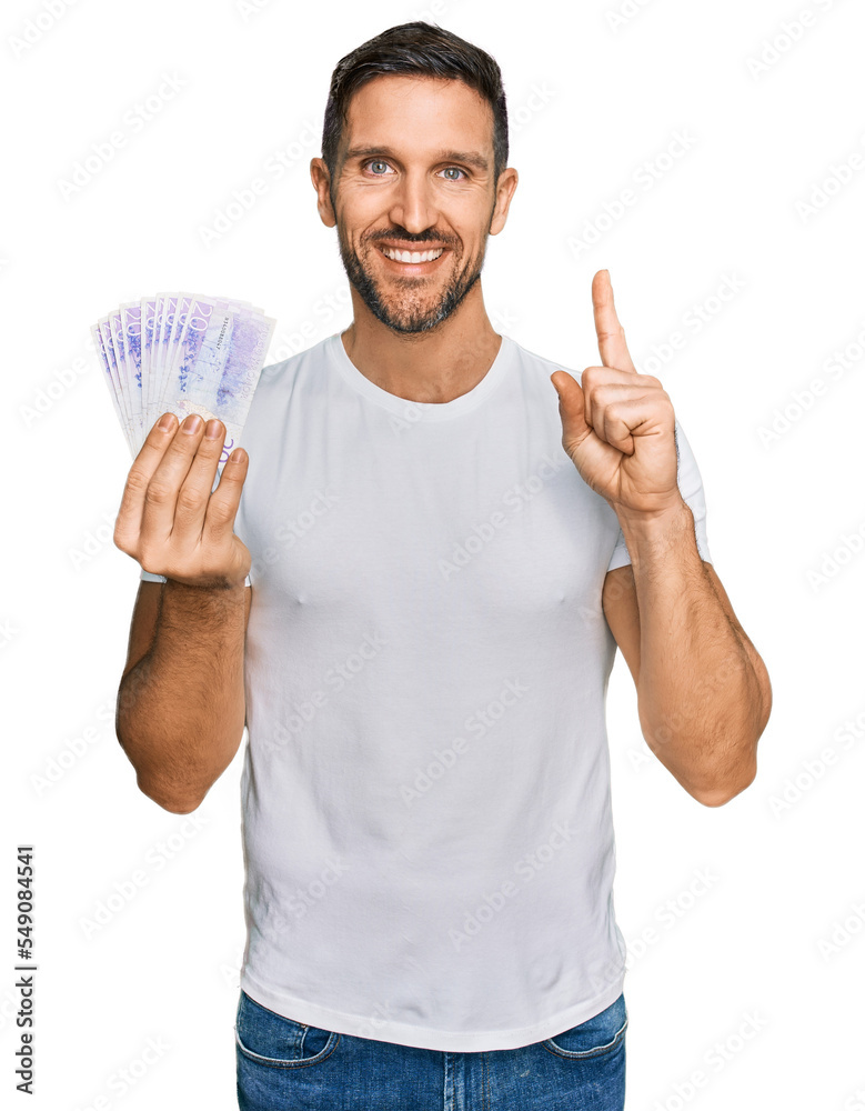 Handsome man with beard holding 20 swedish krona banknotes surprised with an idea or question pointing finger with happy face, number one Handsome man with beard holding 20 swedish krona banknotes surprised with an idea or question pointing finger with happy face, number one