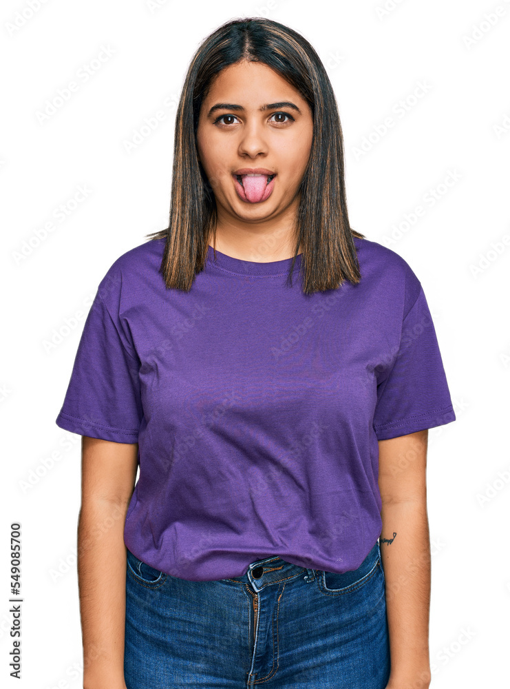 Young hispanic girl wearing casual purple t shirt sticking tongue out happy with funny expression. emotion concept. Young hispanic girl wearing casual purple t shirt sticking tongue out happy with funny expression. emotion concept.