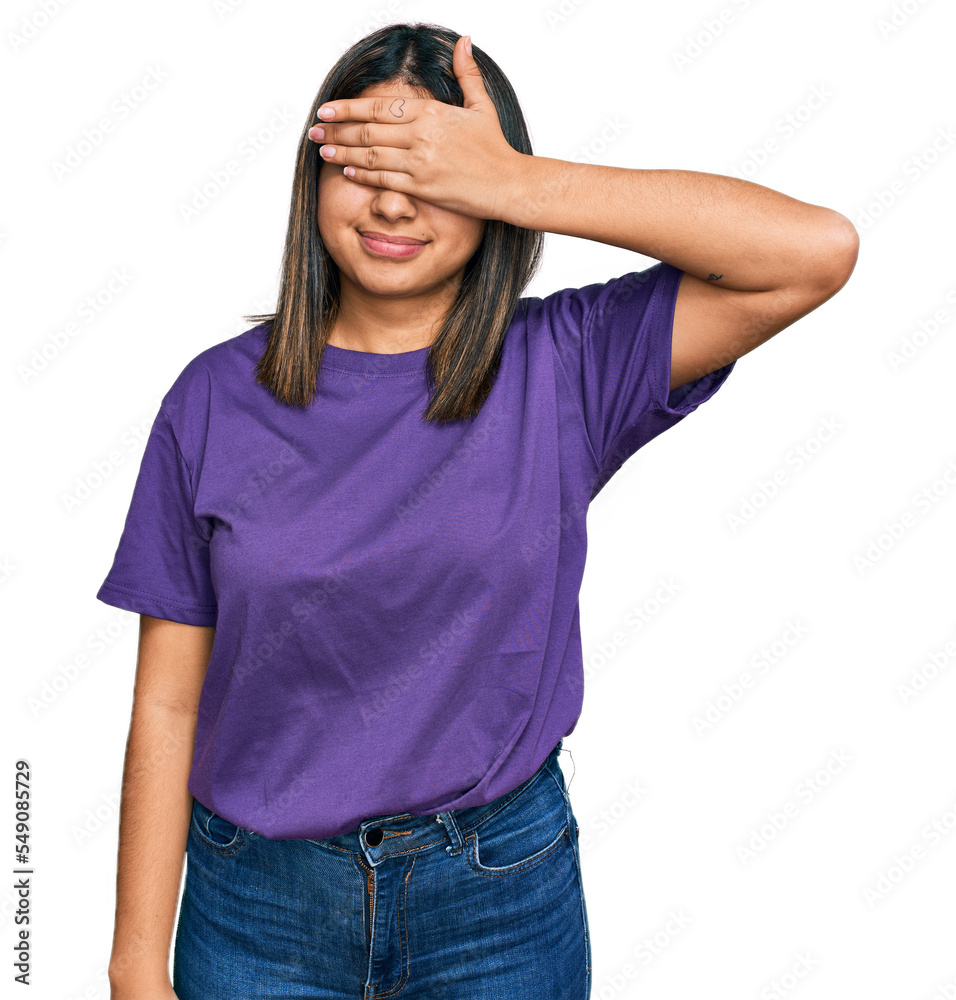 Young hispanic girl wearing casual purple t shirt smiling and laughing with hand on face covering eyes for surprise. blind concept. Young hispanic girl wearing casual purple t shirt smiling and laughing with hand on face covering eyes for surprise. blind concept.