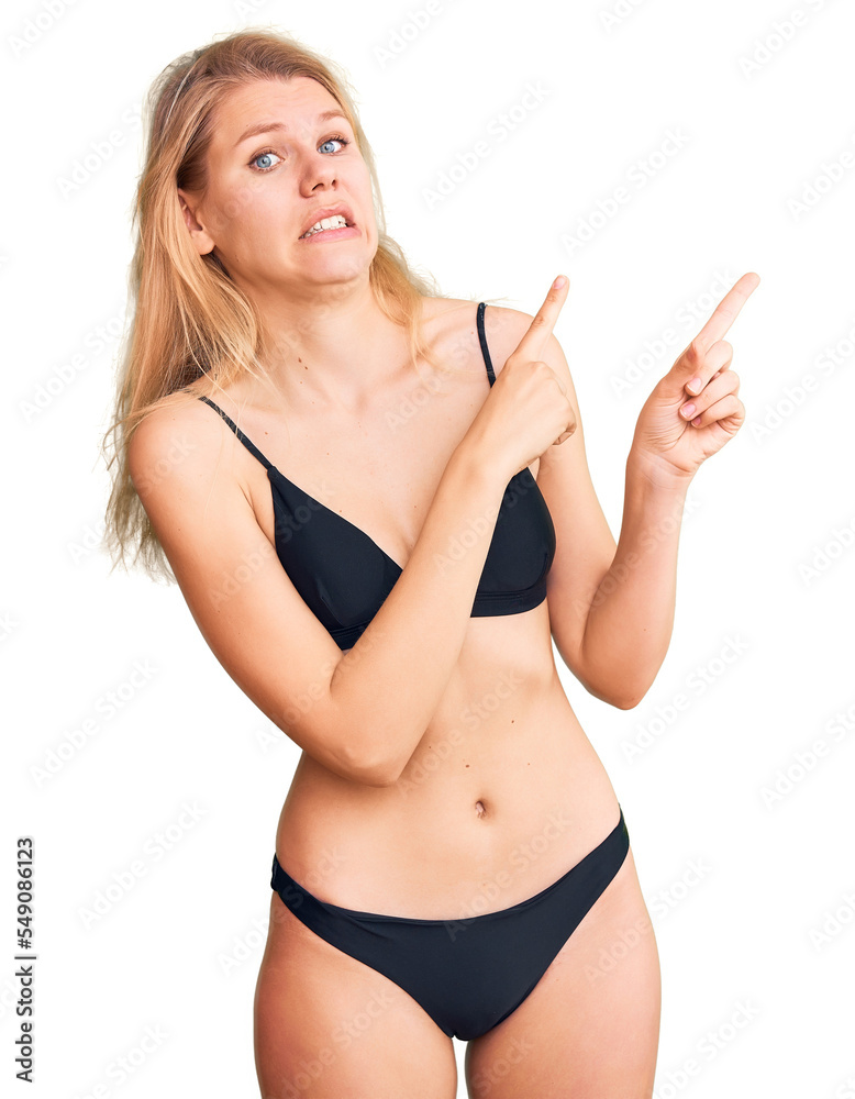 Young beautiful blonde woman wearing bikini pointing aside worried and nervous with both hands, concerned and surprised expression Young beautiful blonde woman wearing bikini pointing aside worried and nervous with both hands, concerned and surprised expression