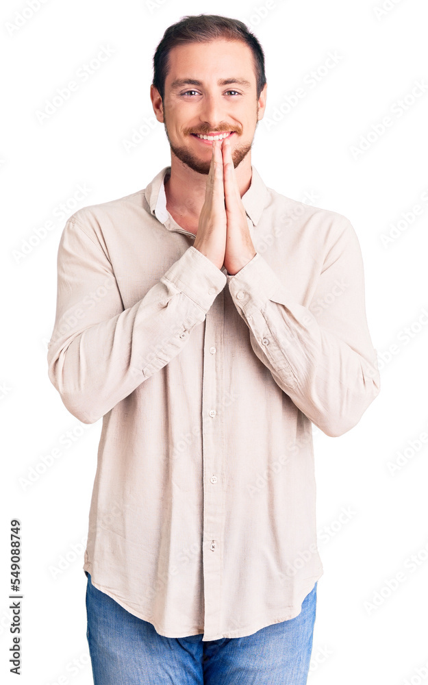 Young handsome caucasian man wearing casual clothes praying with hands together asking for forgiveness smiling confident. Young handsome caucasian man wearing casual clothes praying with hands together asking for forgiveness smiling confident.