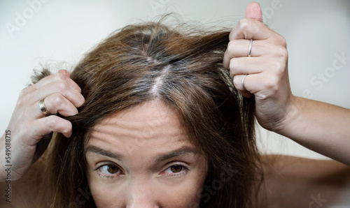 A young woman looks in horror at her gray hair roots in the mirror