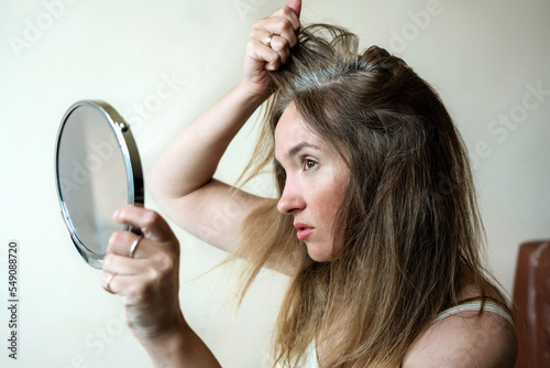 Bild auf Leinwand Young woman looks in the mirror at her gray hair roots