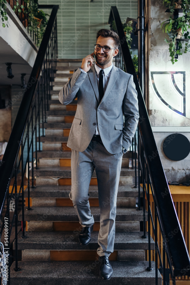 Obraz premium Handsome and smiled middle age businessman using his smart phone while standing in modern office or cafe bar.