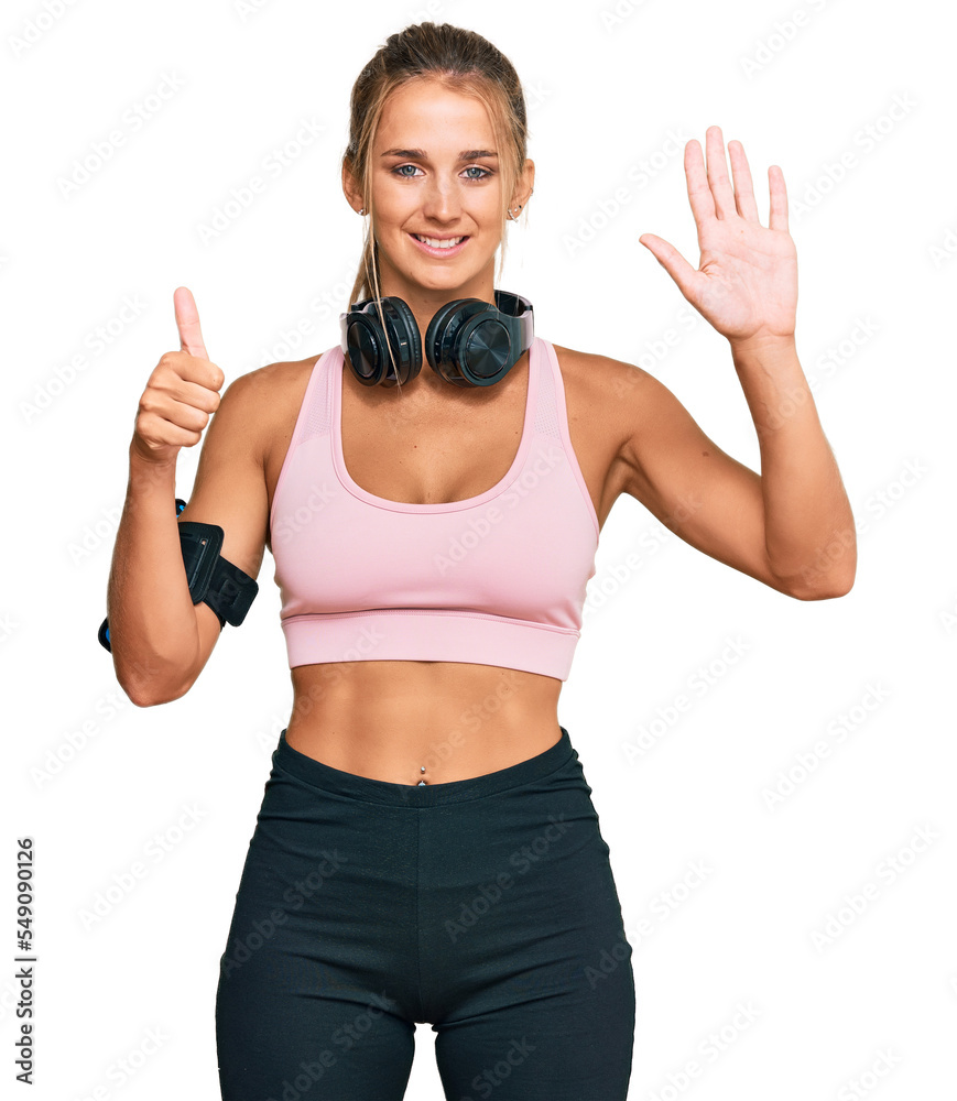 Young blonde woman wearing gym clothes and using headphones showing and pointing up with fingers number six while smiling confident and happy. Young blonde woman wearing gym clothes and using headphones showing and pointing up with fingers number six while smiling confident and happy.