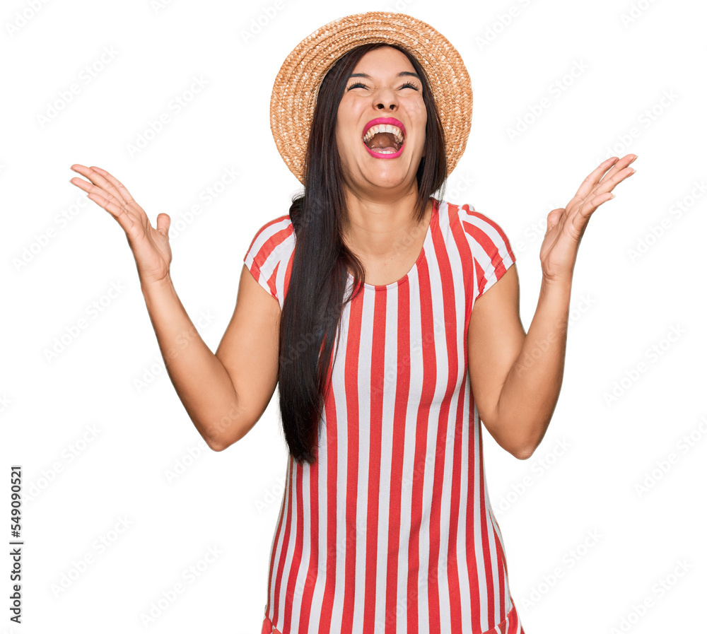 Young hispanic woman wearing summer hat celebrating mad and crazy for success with arms raised and closed eyes screaming excited. winner concept