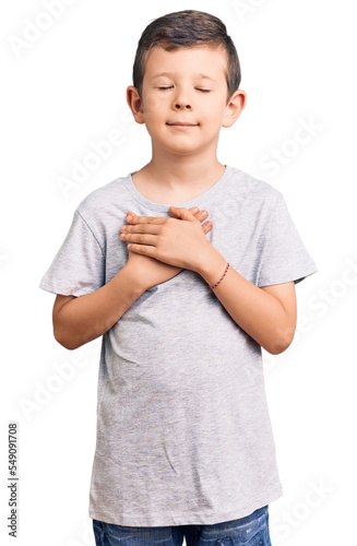 Cute blond kid wearing casual clothes smiling with hands on chest with closed eyes and grateful gesture on face. health concept.