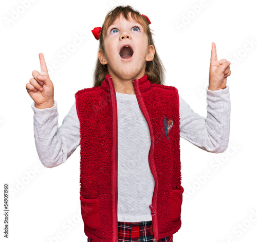 Little caucasian girl kid wearing casual clothes amazed and surprised looking up and pointing with fingers and raised arms.