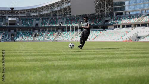 African American man playing football on the stadium field. A man runs with a soccer ball across the field. © Katsiaryna