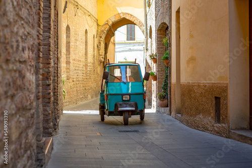 Fototapeta Naklejka Na Ścianę i Meble -  Man in a azul blue tricycle driving in the narrow streets of old italian town of Spello in Perugia.