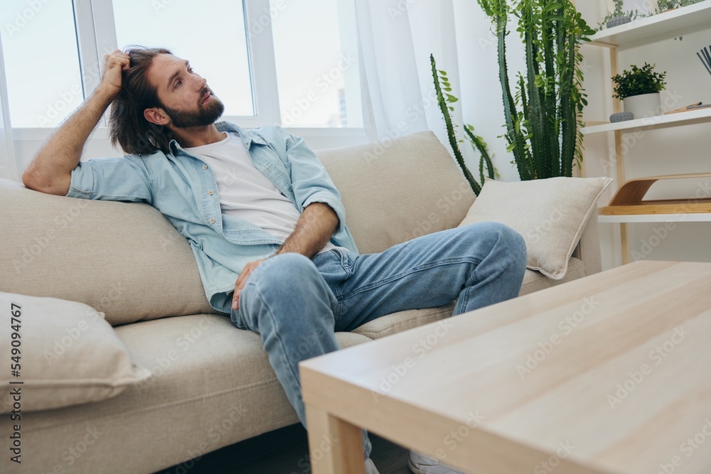 A young male freelancer sits on the couch after a demanding job and rests sadly leaning on the couch. A young male freelancer sits on the couch after a demanding job and rests sadly leaning on the couch.