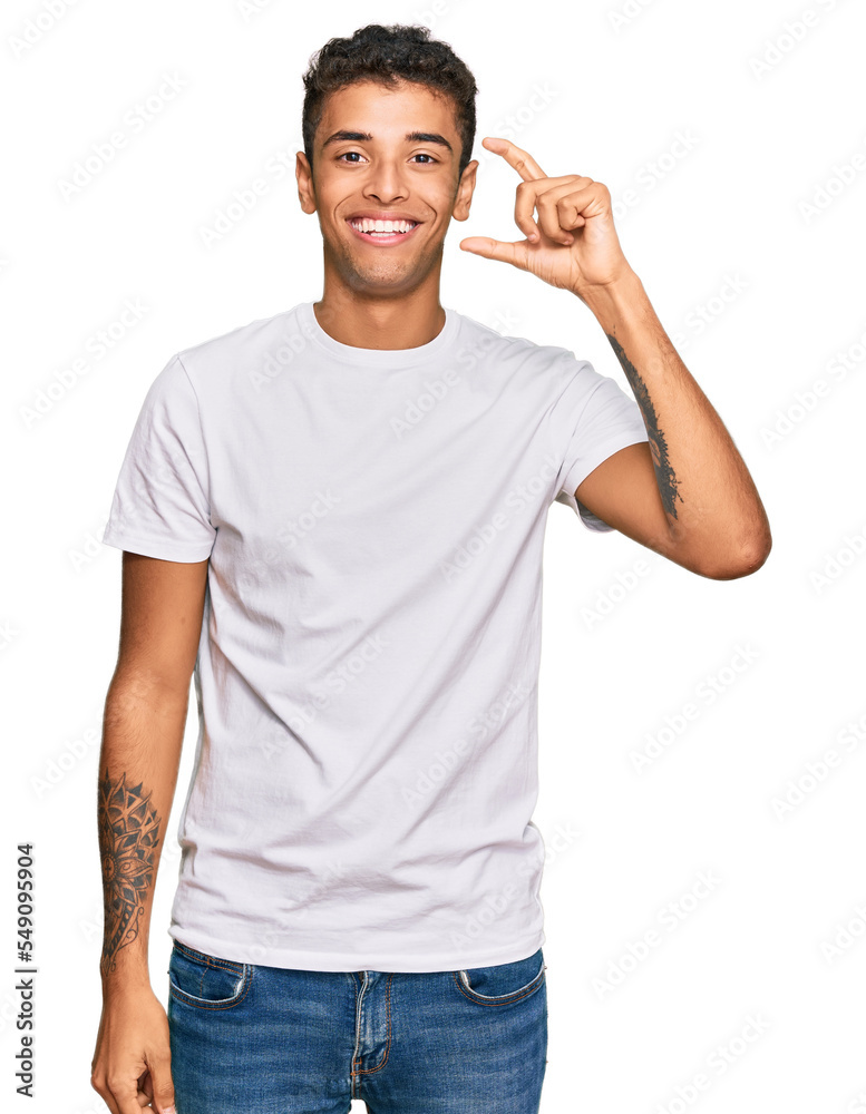 Young handsome african american man wearing casual white tshirt smiling and confident gesturing with hand doing small size sign with fingers looking and the camera. measure concept. Young handsome african american man wearing casual white tshirt smiling and confident gesturing with hand doing small size sign with fingers looking and the camera. measure concept.