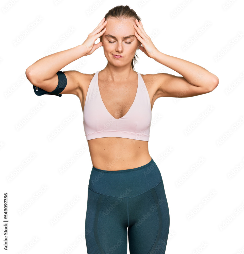Beautiful young blonde woman wearing sportswear and arm band suffering from headache desperate and stressed because pain and migraine. hands on head. Beautiful young blonde woman wearing sportswear and arm band suffering from headache desperate and stressed because pain and migraine. hands on head.
