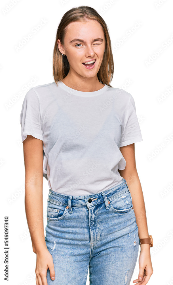 Obraz premium Beautiful young blonde woman wearing casual white t shirt winking looking at the camera with sexy expression, cheerful and happy face.