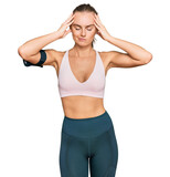 Beautiful young blonde woman wearing sportswear and arm band suffering from headache desperate and stressed because pain and migraine. hands on head.