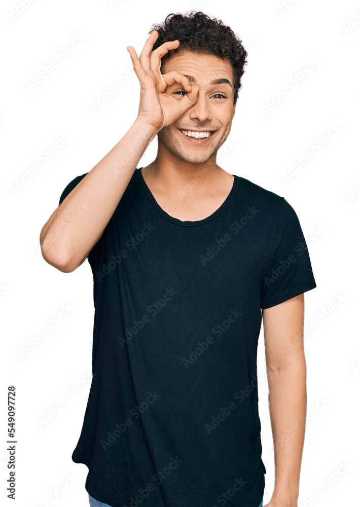 Young handsome man wearing casual black t shirt doing ok gesture with hand smiling, eye looking through fingers with happy face. Young handsome man wearing casual black t shirt doing ok gesture with hand smiling, eye looking through fingers with happy face.