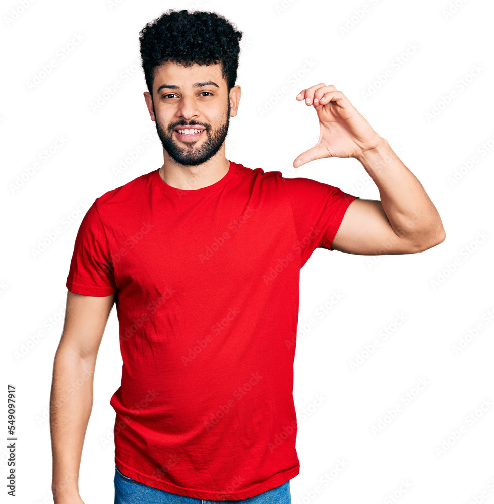 Young arab man with beard wearing casual red t shirt smiling and confident gesturing with hand doing small size sign with fingers looking and the camera. measure concept. Young arab man with beard wearing casual red t shirt smiling and confident gesturing with hand doing small size sign with fingers looking and the camera. measure concept.