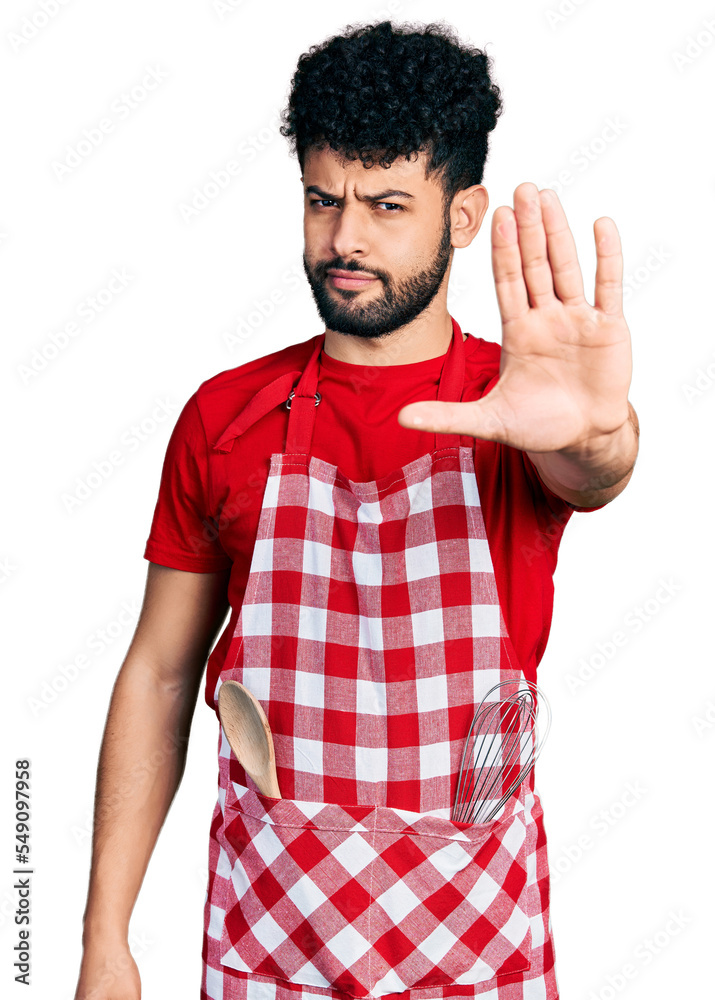 Young arab man with beard wearing cook apron doing stop sing with palm of the hand. warning expression with negative and serious gesture on the face. Young arab man with beard wearing cook apron doing stop sing with palm of the hand. warning expression with negative and serious gesture on the face.