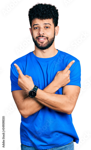 Young arab man with beard wearing casual blue t shirt pointing to both sides with fingers, different direction disagree