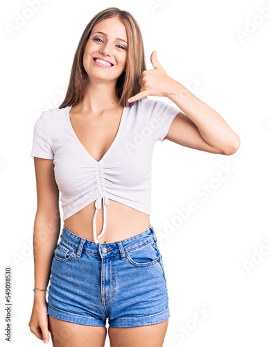 Young beautiful blonde woman wearing casual white tshirt smiling doing phone gesture with hand and fingers like talking on the telephone. communicating concepts.