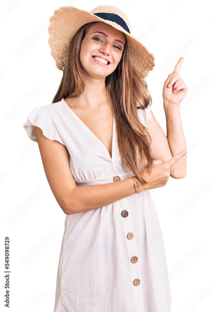 Young beautiful blonde woman wearing summer dress and hat smiling and looking at the camera pointing with two hands and fingers to the side. Young beautiful blonde woman wearing summer dress and hat smiling and looking at the camera pointing with two hands and fingers to the side.