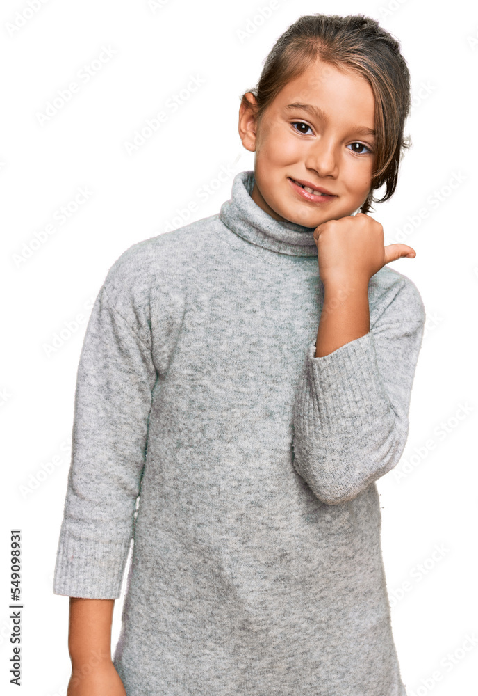 Little beautiful girl wearing casual turtleneck sweater smiling with happy face looking and pointing to the side with thumb up. Little beautiful girl wearing casual turtleneck sweater smiling with happy face looking and pointing to the side with thumb up.