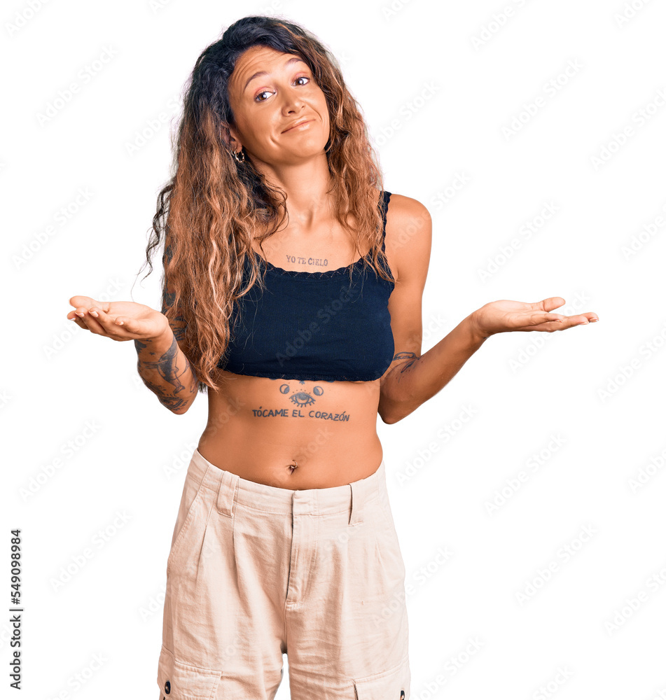 Young hispanic woman with tattoo wearing casual clothes clueless and confused expression with arms and hands raised. doubt concept. Young hispanic woman with tattoo wearing casual clothes clueless and confused expression with arms and hands raised. doubt concept.