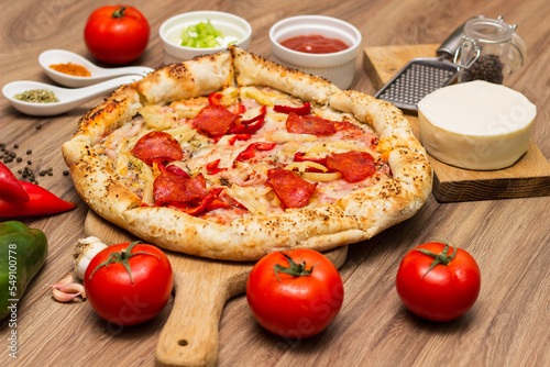 Tasty pizza with pepperoni, ham and peppers and pizza ingredients around the table