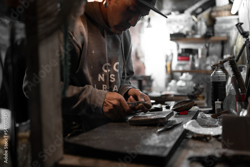 A craftsman jeweler is cutting a metal piece to create a jewel