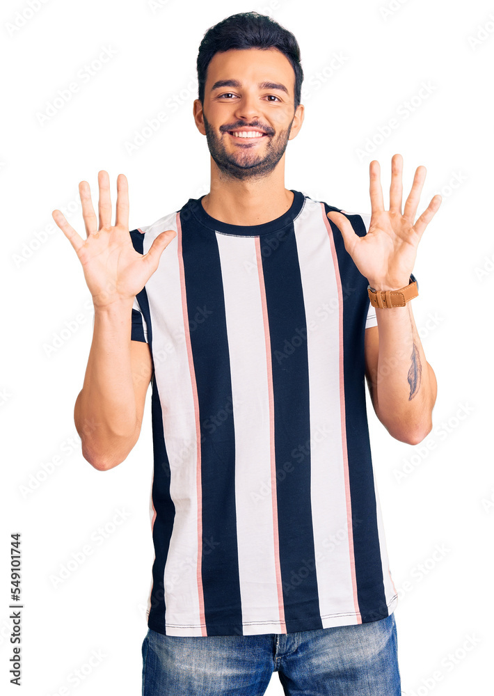 Naklejka premium Young handsome hispanic man wearing striped tshirt showing and pointing up with fingers number ten while smiling confident and happy.