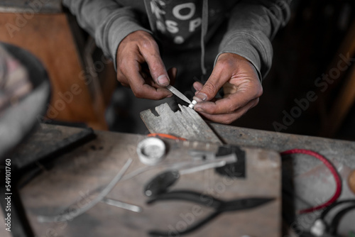 A craftsman jeweler is using a file tool to create a small metal jewel piece