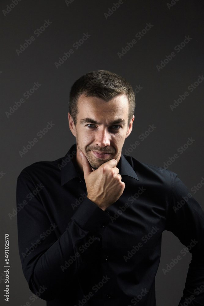 Portrait of pensive man in a black shirt on a dark background. Young caucasian dark-haired man Portrait of pensive man in a black shirt on a dark background. Young caucasian dark-haired man