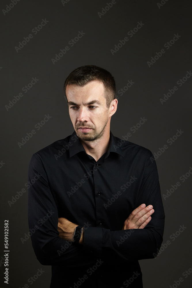 Portrait of man in a black shirt on a dark background. Serious brunet with arms folded. Young caucasian man