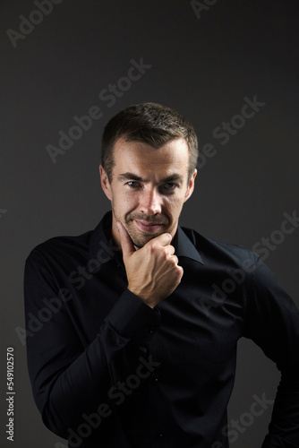 Portrait of pensive man in a black shirt on a dark background. Young caucasian dark-haired man