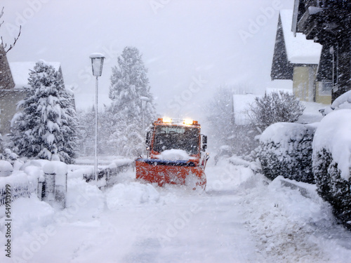 Mittersill, Austria - Orange truck with snow chains and plow clears snow in mountain city. Snow disaster in the Alps.