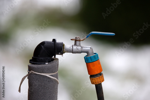 Water tap faucet with hosepipe attached and blue handle closed in winter garden 