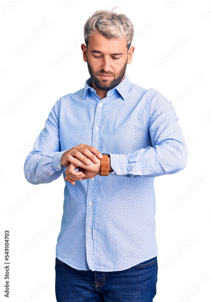 Young handsome blond man wearing elegant shirt checking the time on wrist watch, relaxed and confident
