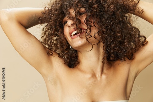 Woman applies cream and balm to her curly hair, the concept of protection and care, a healthy look, a smile with teeth on a beige background