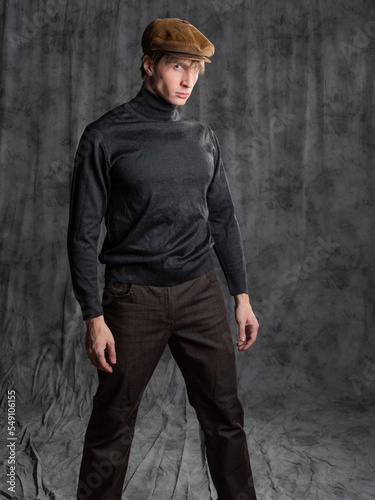 Retro character in the style of the 60s. A young man in a flat cap and a black turtleneck. Posing in the studio on a gray background