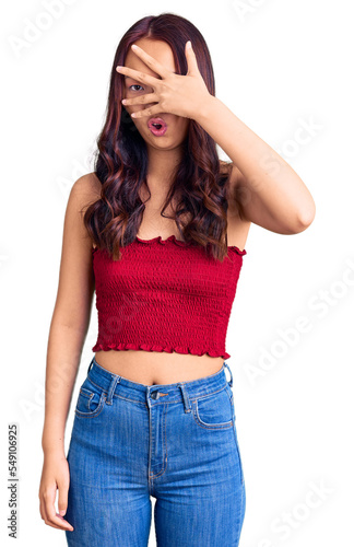 Young beautiful chinese girl wearing casual clothes peeking in shock covering face and eyes with hand, looking through fingers with embarrassed expression.