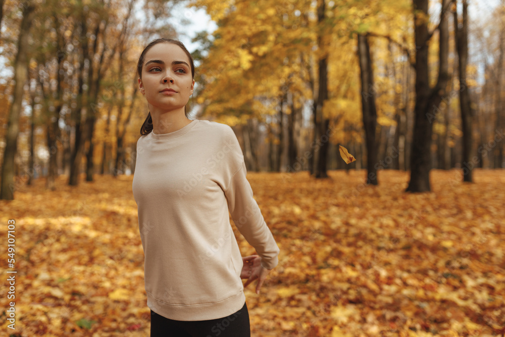Fit female athlete stretching arms behind back while exercising during fitness workout in autumn in nature Fit female athlete stretching arms behind back while exercising during fitness workout in autumn in nature