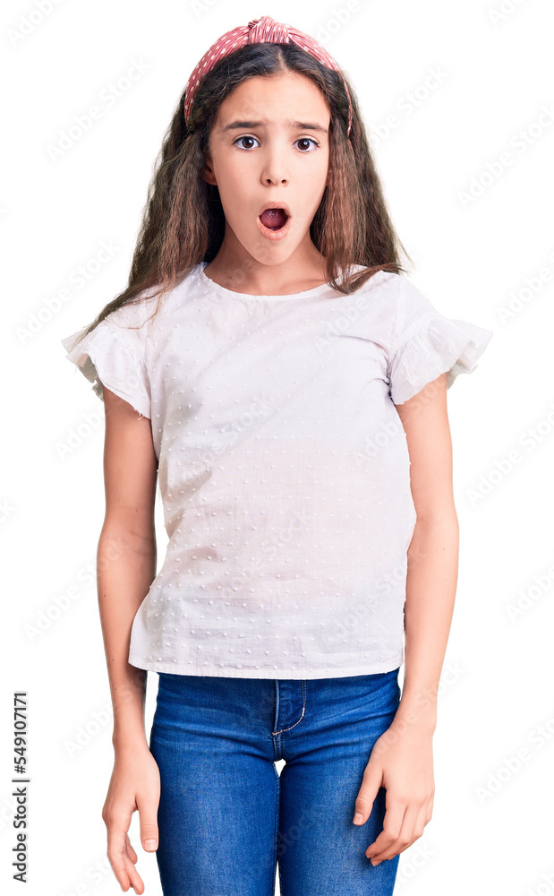 Obraz premium Cute hispanic child girl wearing casual white tshirt in shock face, looking skeptical and sarcastic, surprised with open mouth