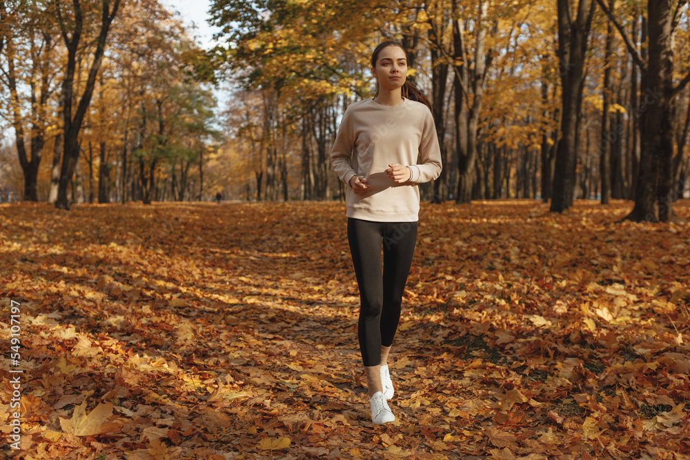 Full body of sporty woman running in autumn park during training in autumn on sunny day Full body of sporty woman running in autumn park during training in autumn on sunny day
