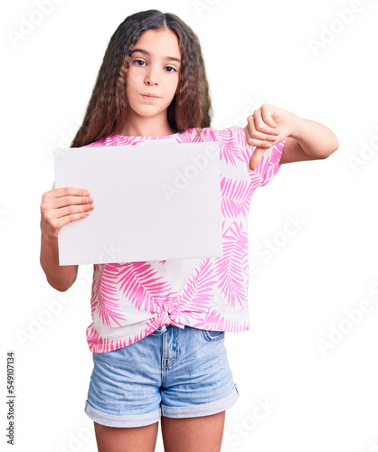 Cute hispanic child girl holding blank empty banner with angry face, negative sign showing dislike with thumbs down, rejection concept